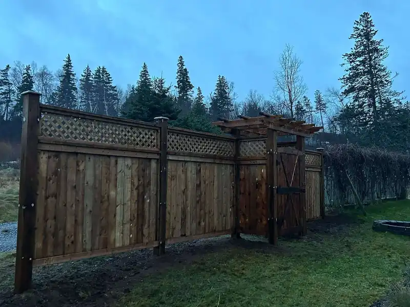 A run of cedar privacy fence with a lattice top along a treed property line.