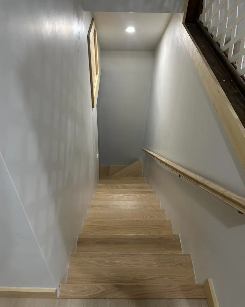 A staircase with oak treads and white risers between plastered walls.