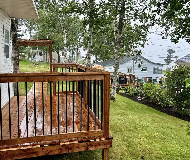 A timber deck with a black picket rail looking out over a lawn and houses.