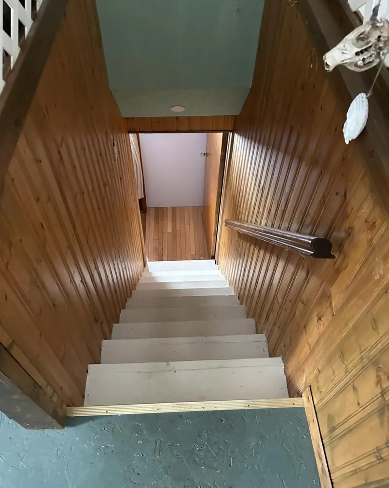 A stairwell lined in vertical pine boards, looking down to the landing.
