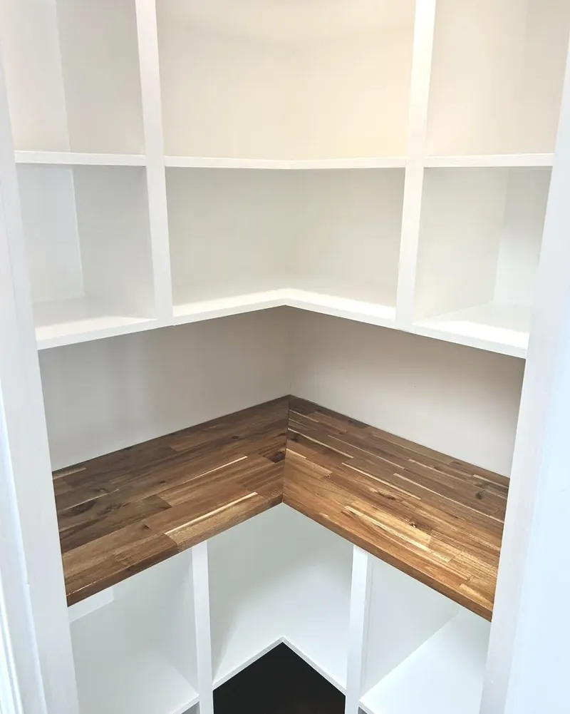 White built-in shelving wrapping a corner above a walnut window sill.