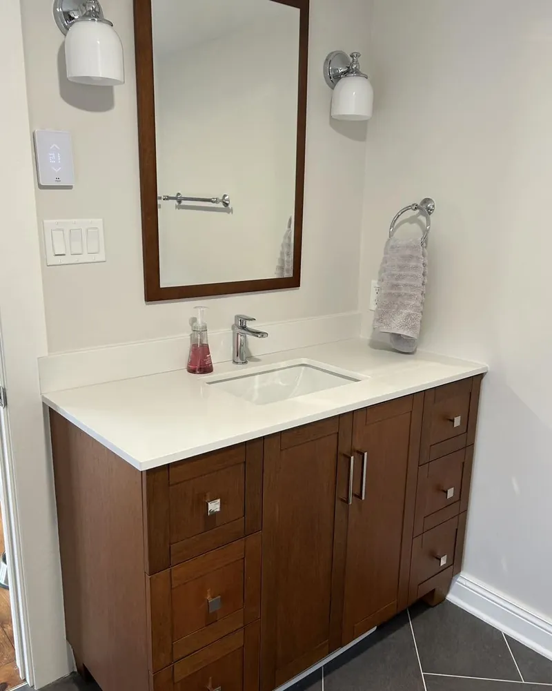 A dark wood vanity with a stone top, mirror and sconce above.