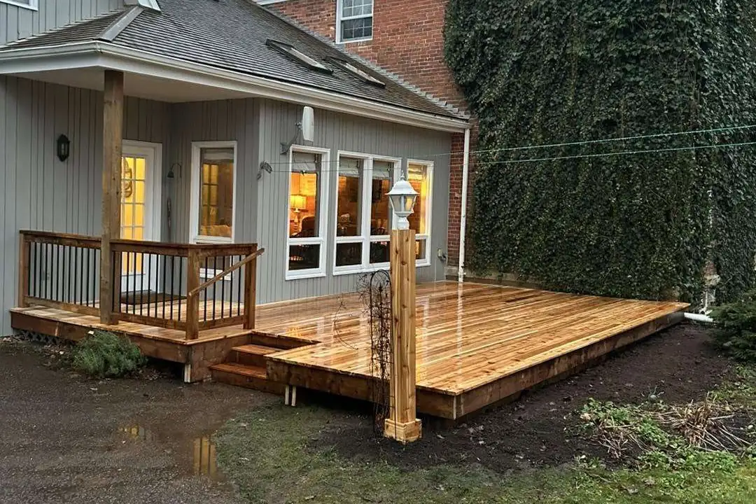 A finished cedar deck off the back of a house at dusk, with the lights on inside.