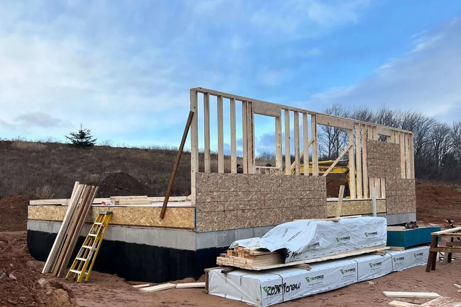 First-floor walls standing on a new foundation, with sheathing and framing stock stacked alongside.