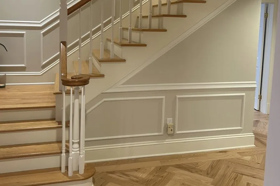 A stair hall with painted panelled wainscot and trim, oak treads and a herringbone floor.